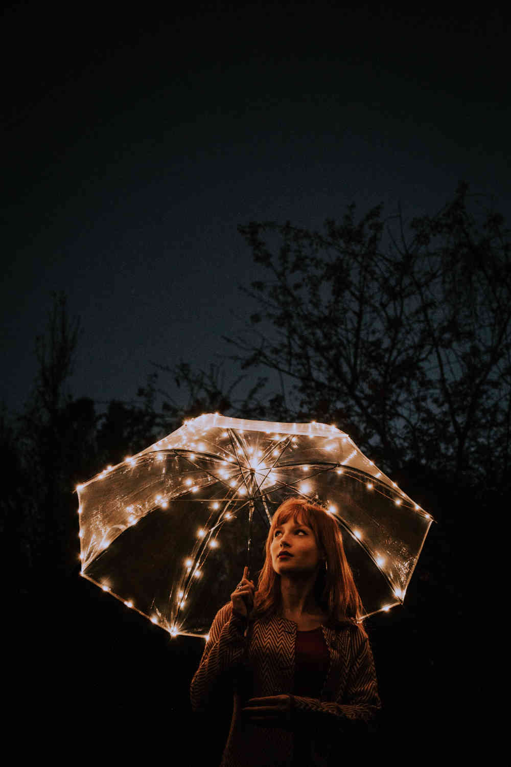 Woman amid darkness holding up an umbrella - that illuminates her from its many tiny lights.